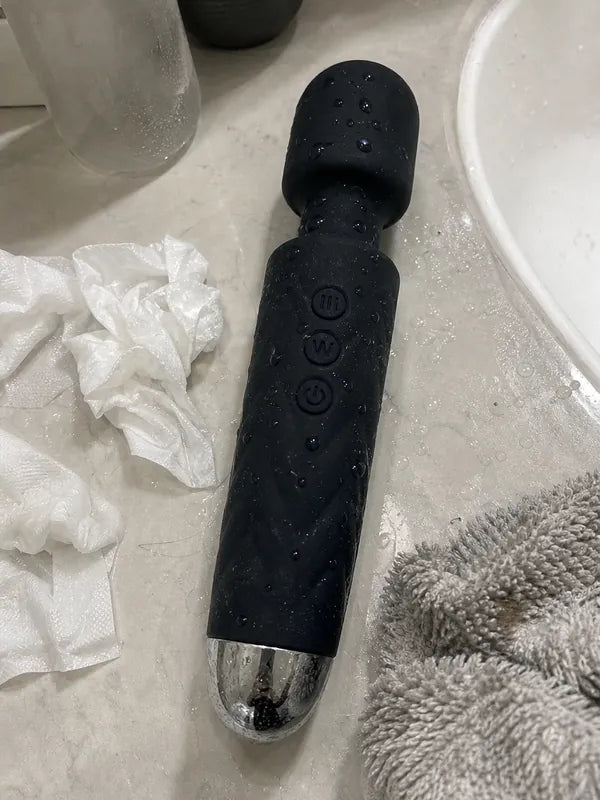 Large black wand vibrator left wet on a bathroom counter with tissues and towel nearby