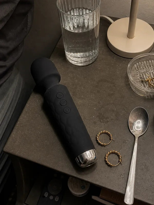 Bulky black wand vibrator left out on a bedside table